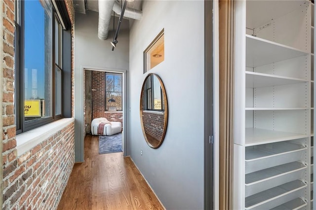 hall featuring a wealth of natural light, wood-type flooring, and brick wall