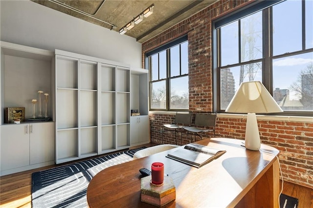 office area with hardwood / wood-style flooring, brick wall, and track lighting