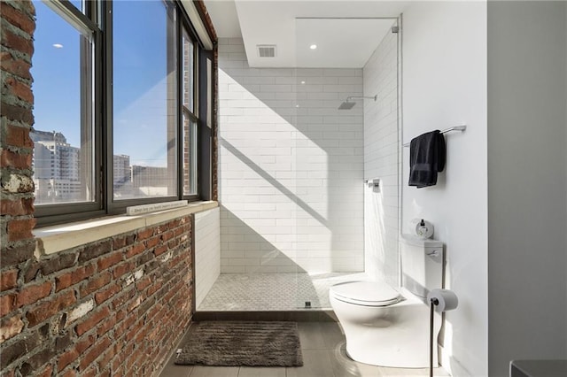 bathroom featuring tiled shower, tile patterned floors, toilet, and brick wall