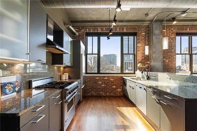 kitchen with brick wall, stainless steel appliances, sink, and dark stone counters