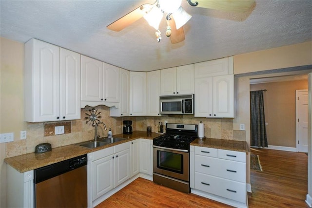 kitchen with sink, appliances with stainless steel finishes, white cabinets, decorative backsplash, and light wood-type flooring