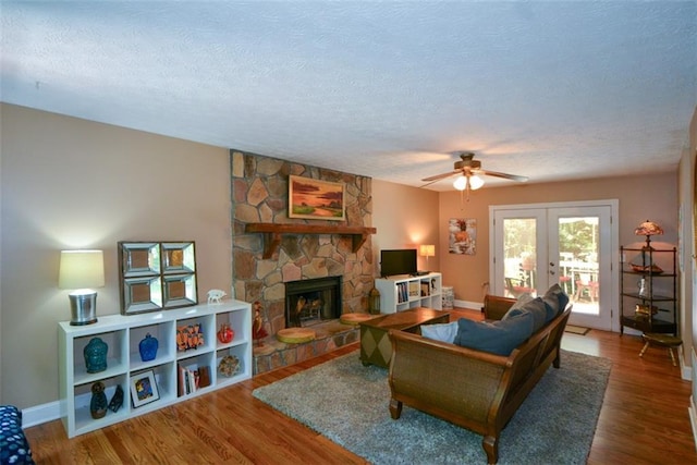 living room with a stone fireplace, french doors, a textured ceiling, and hardwood / wood-style flooring