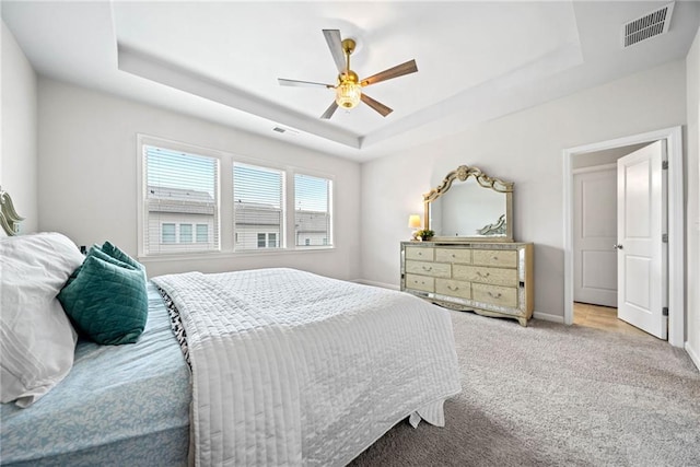 carpeted bedroom featuring ceiling fan, a tray ceiling, and visible vents