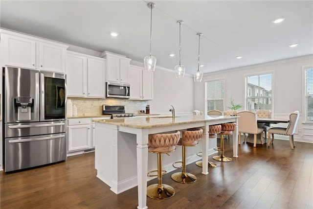 kitchen featuring dark wood-style floors, tasteful backsplash, appliances with stainless steel finishes, ornamental molding, and an island with sink