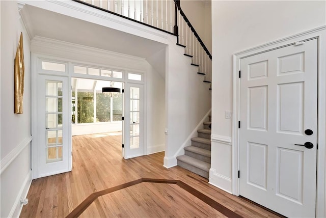 foyer entrance featuring crown molding, baseboards, stairway, a towering ceiling, and wood finished floors