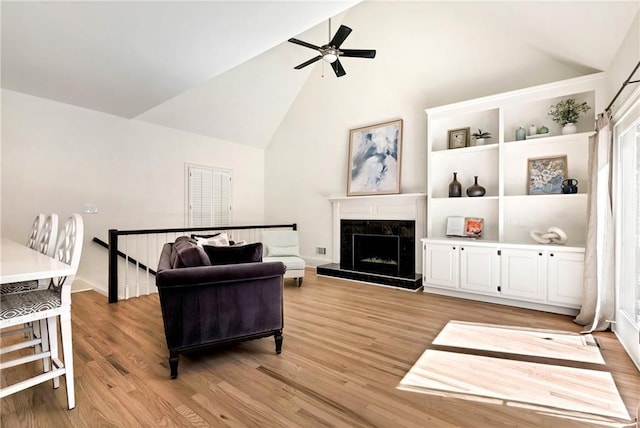 living room featuring high vaulted ceiling, a fireplace, light wood finished floors, and ceiling fan