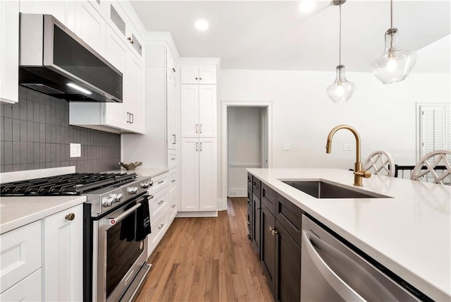 kitchen featuring range hood, a sink, stainless steel appliances, light countertops, and white cabinets