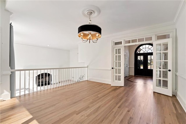 empty room featuring baseboards, ornamental molding, french doors, an inviting chandelier, and wood finished floors