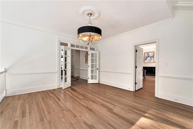 unfurnished dining area featuring french doors, wood finished floors, a notable chandelier, and ornamental molding