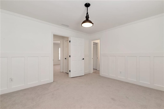 unfurnished room with visible vents, crown molding, a wainscoted wall, light colored carpet, and a decorative wall