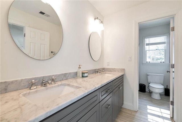 full bathroom with double vanity, toilet, visible vents, and a sink