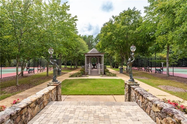 view of property's community featuring a tennis court, a lawn, and fence