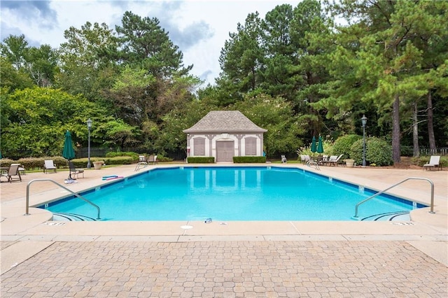 pool with a patio area, an outdoor structure, and fence