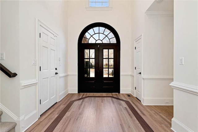 entrance foyer with arched walkways, french doors, stairs, and wood finished floors