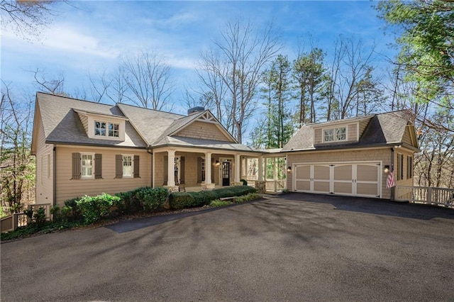 view of front facade featuring an outbuilding, aphalt driveway, a porch, an attached garage, and roof with shingles