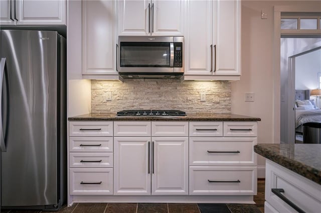 kitchen featuring white cabinets, tasteful backsplash, stainless steel appliances, and dark stone countertops