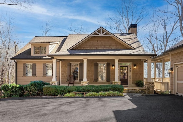 craftsman house featuring roof with shingles, a porch, and a chimney