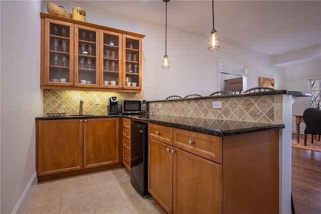 kitchen with a peninsula, decorative backsplash, brown cabinets, dark stone counters, and stainless steel microwave