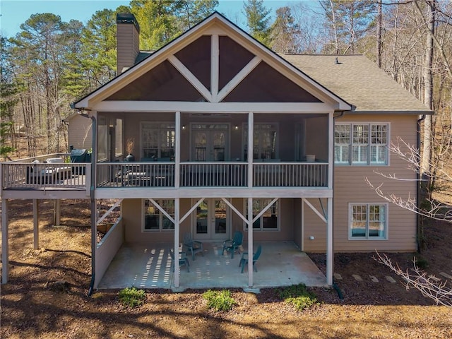 back of house featuring a shingled roof, a sunroom, french doors, a chimney, and a patio area