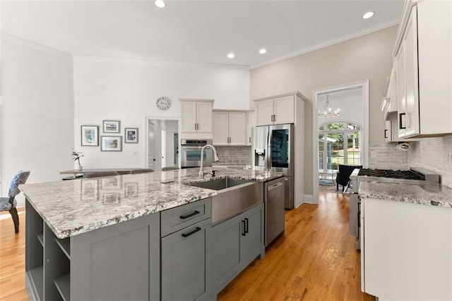 kitchen featuring appliances with stainless steel finishes, backsplash, gray cabinets, and an island with sink