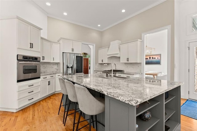 kitchen with custom range hood, stainless steel appliances, white cabinetry, and a center island with sink