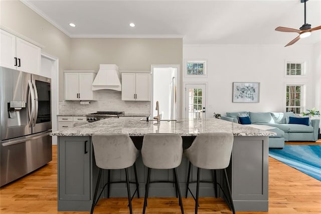 kitchen featuring white cabinets, a spacious island, stainless steel fridge with ice dispenser, and premium range hood