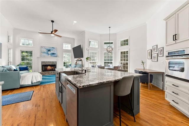 kitchen featuring a center island with sink, sink, hanging light fixtures, a brick fireplace, and stainless steel appliances