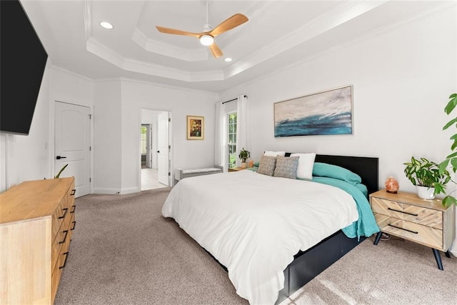 carpeted bedroom with ceiling fan, a raised ceiling, ornamental molding, and ensuite bath