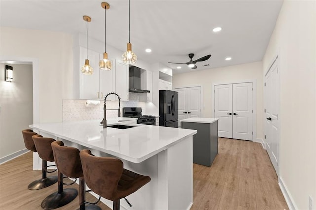 kitchen with wall chimney range hood, kitchen peninsula, pendant lighting, a breakfast bar area, and black appliances