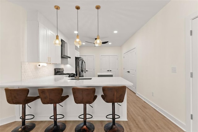 kitchen with white cabinets, hanging light fixtures, appliances with stainless steel finishes, a kitchen bar, and kitchen peninsula