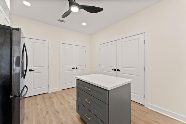 interior space with stainless steel refrigerator, ceiling fan, a center island, gray cabinetry, and light hardwood / wood-style flooring