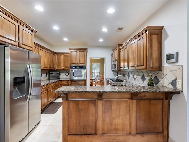 11 Stillwater Way, Hoschton, GA 30548 - kitchen featuring appliances with stainless steel finishes, a peninsula, backsplash, recessed lighting, and brown cabinetry