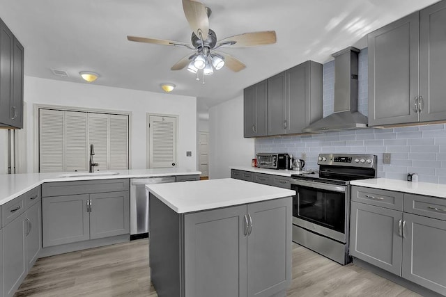 kitchen with gray cabinetry, sink, stainless steel appliances, and wall chimney range hood