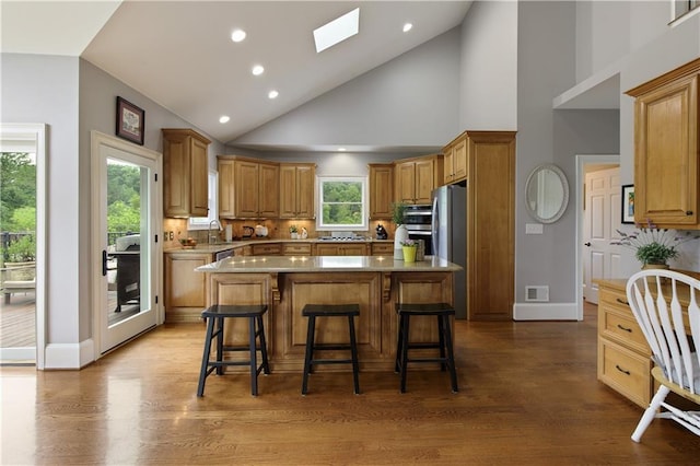 2675 Portabella Ln, Cumming, GA 30041 - kitchen featuring stainless steel appliances, wood finished floors, decorative backsplash, a breakfast bar area, and a center island