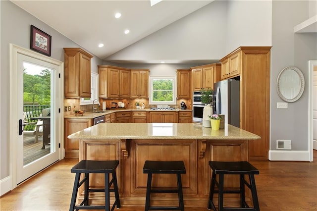 2675 Portabella Ln, Cumming, GA 30041 - kitchen featuring appliances with stainless steel finishes, wood finished floors, light stone counters, backsplash, and a sink