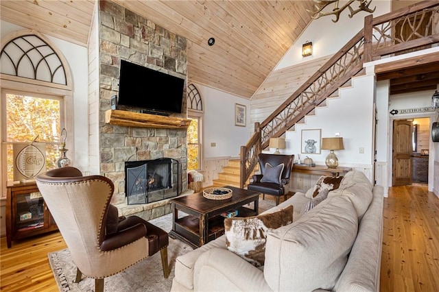 living room with high vaulted ceiling, wooden ceiling, a stone fireplace, and light hardwood / wood-style flooring