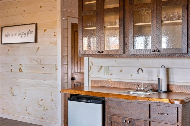 kitchen with wood-type flooring, sink, wooden walls, and dishwasher