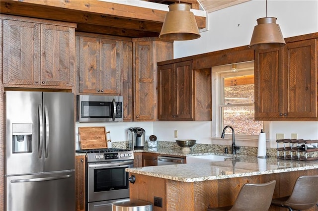 kitchen with stainless steel appliances, stone counters, hanging light fixtures, sink, and a breakfast bar area