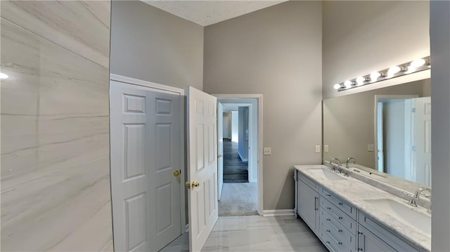 full bath featuring baseboards, a sink, a high ceiling, and double vanity