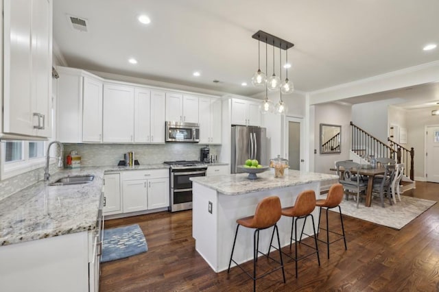 kitchen featuring tasteful backsplash, a kitchen island, stainless steel appliances, white cabinetry, and a sink