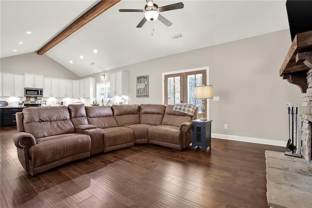 living room with dark hardwood / wood-style flooring, a stone fireplace, a wealth of natural light, and beamed ceiling