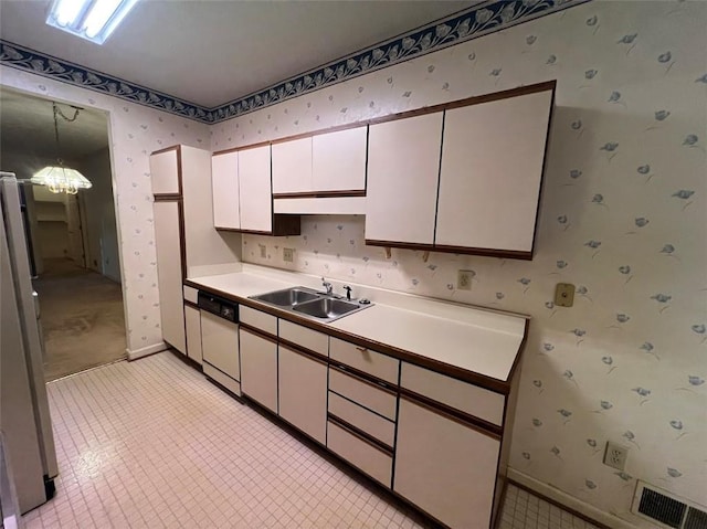 kitchen with wallpapered walls, freestanding refrigerator, white dishwasher, white cabinetry, and a sink