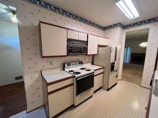 kitchen featuring light countertops, a fireplace with raised hearth, white cabinets, white appliances, and wallpapered walls