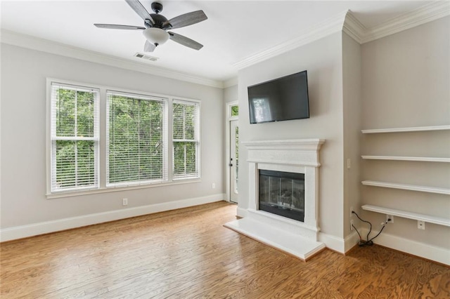 unfurnished living room featuring crown molding, wood finished floors, a glass covered fireplace, a ceiling fan, and baseboards