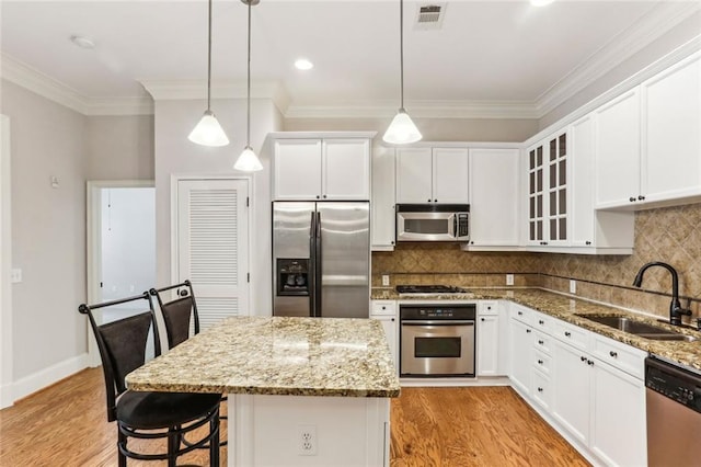 kitchen featuring stainless steel appliances, a sink, light wood finished floors, white cabinets, and ornamental molding