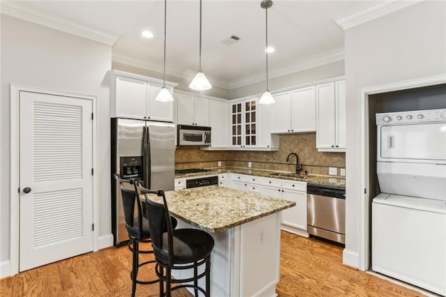 kitchen featuring stainless steel appliances, stacked washer and clothes dryer, a sink, decorative backsplash, and ornamental molding