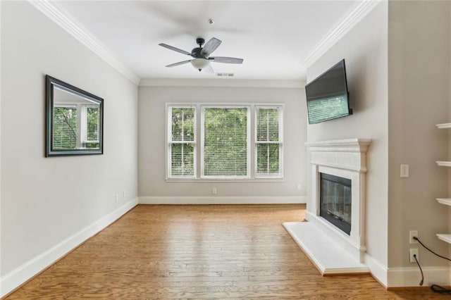 unfurnished living room with crown molding, a glass covered fireplace, a ceiling fan, wood finished floors, and baseboards