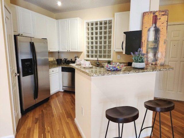 kitchen featuring appliances with stainless steel finishes, light hardwood / wood-style flooring, light stone counters, kitchen peninsula, and white cabinetry