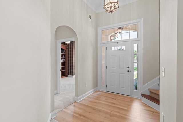 entrance foyer with a high ceiling, ornamental molding, a chandelier, and light hardwood / wood-style floors