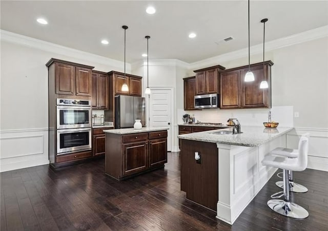 kitchen featuring sink, light stone counters, hanging light fixtures, kitchen peninsula, and stainless steel appliances